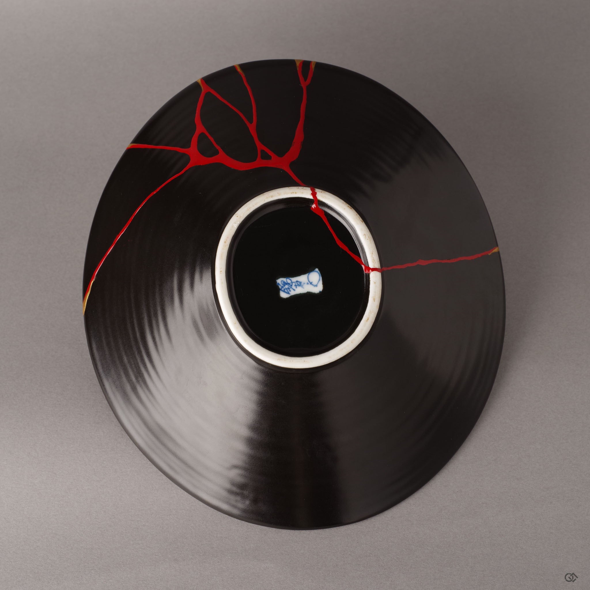 The underside of an Arita ware bowl, revealing the artisan's mark and vermillion iro-urushitsugi repair—a quiet crimson counterpart to the golden restoration on the surface.