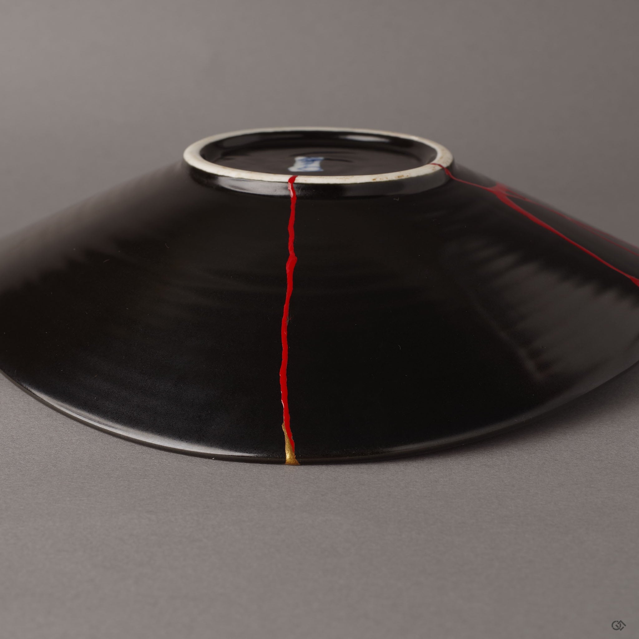 A close-up of the vermillion iro-urushitsugi repair on the reverse of an Arita ware bowl—quiet crimson lines tracing a path of resilience beneath the golden surface.