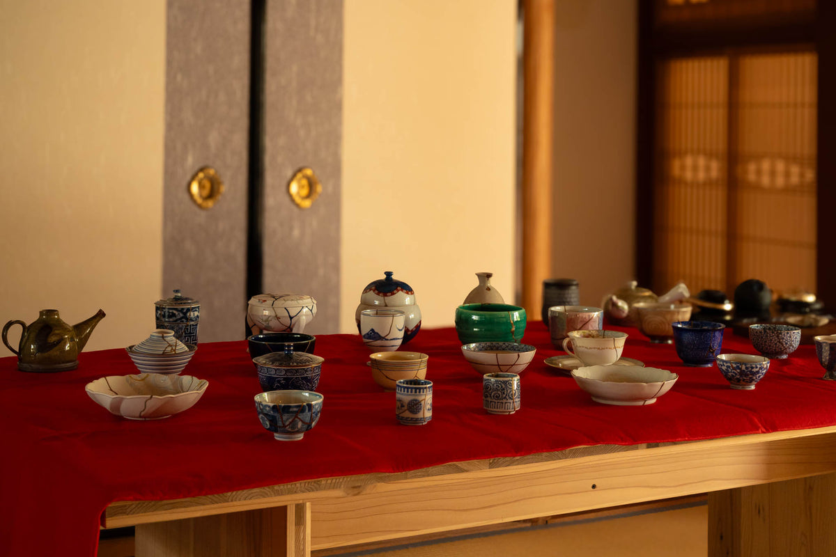 Authentic kintsugi tea bowls, cups and teapots with gold urushi repairs displayed on a red cloth in a Japanese tatami room