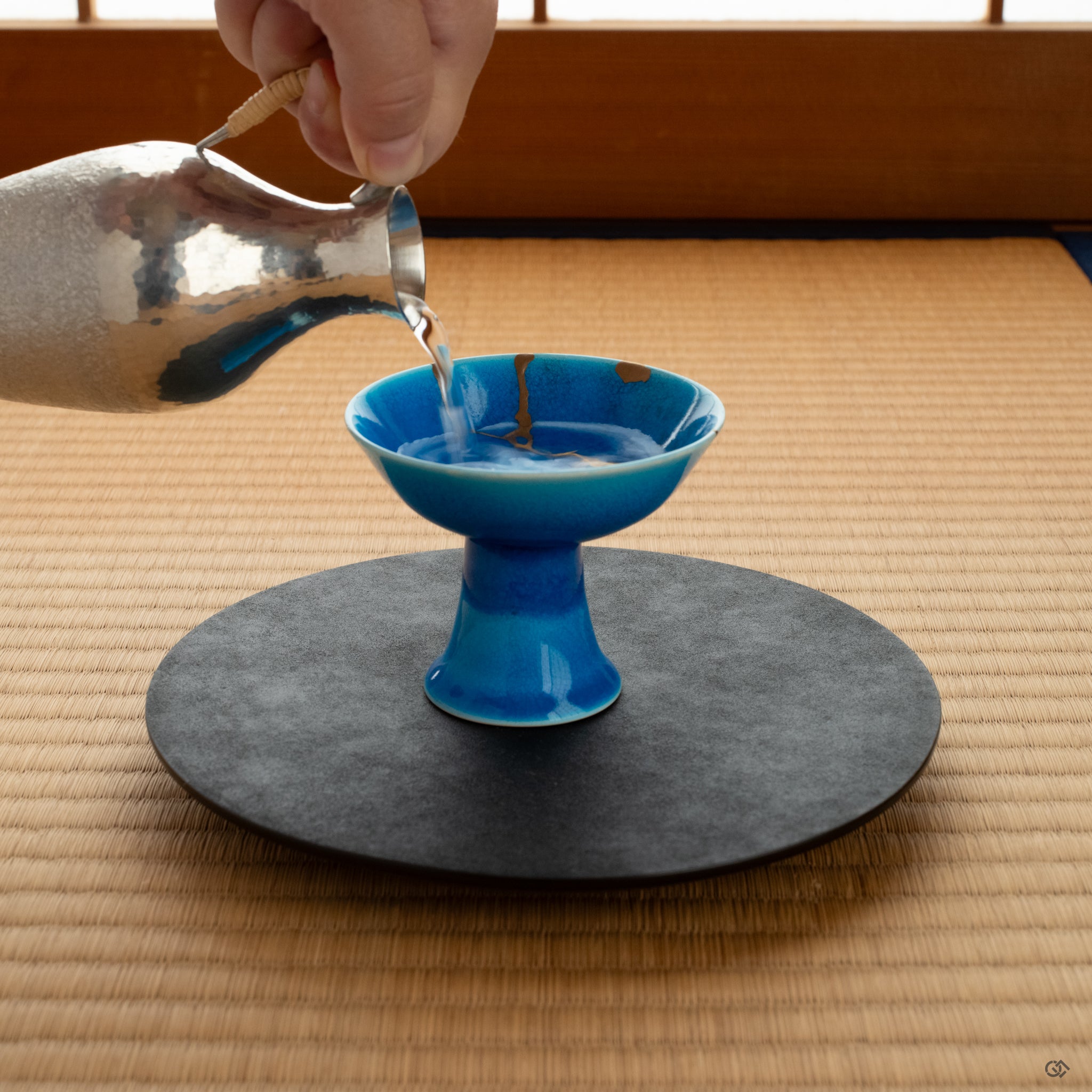A kintsugi Arita sake cup on a tatami mat, restored with urushi lacquer and 24K gold, embodying conscious luxury and a quiet beauty.