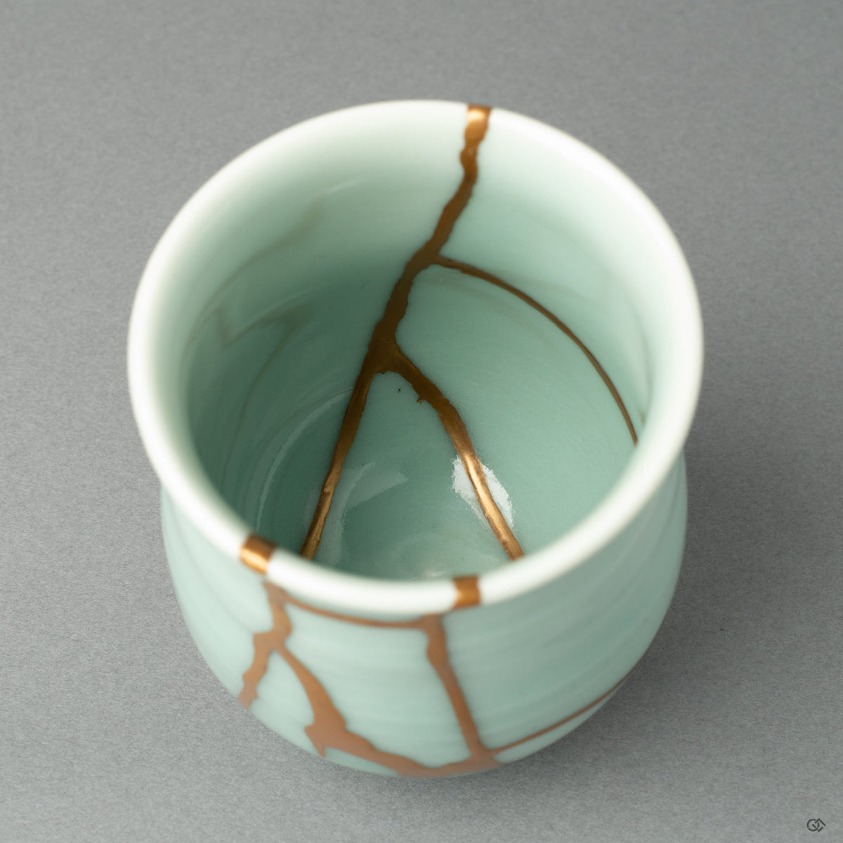 A detail shot focusing on the texture of the 24k gold seam as it meets the fine, glassy celadon glaze of the Nabeshima ware porcelain.