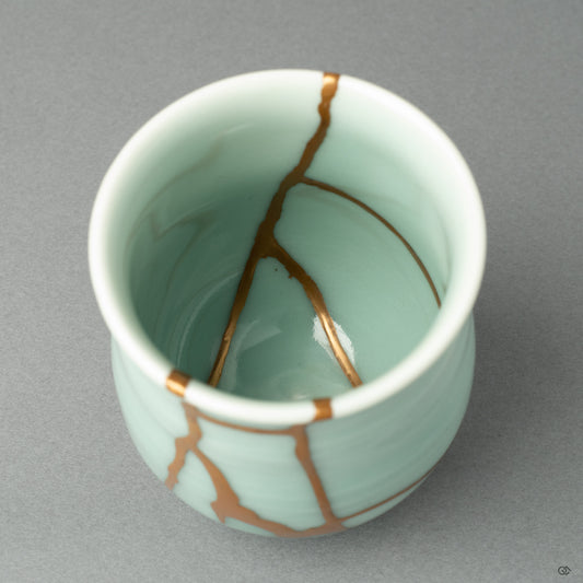 A detail shot focusing on the texture of the 24k gold seam as it meets the fine, glassy celadon glaze of the Nabeshima ware porcelain.
