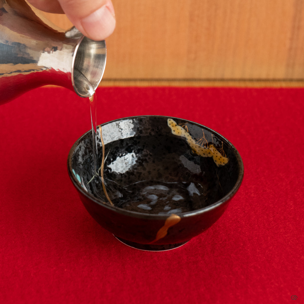 The kintsugi Arita cup, put on the red color felt for puring a sip of sake, a restored and soulful object that enriches the moment.