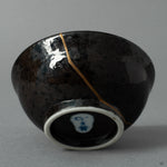 The shining 24K gold kintsugi seam on the ceramic surface, a quiet moment where the vessels journey becomes history made visible.