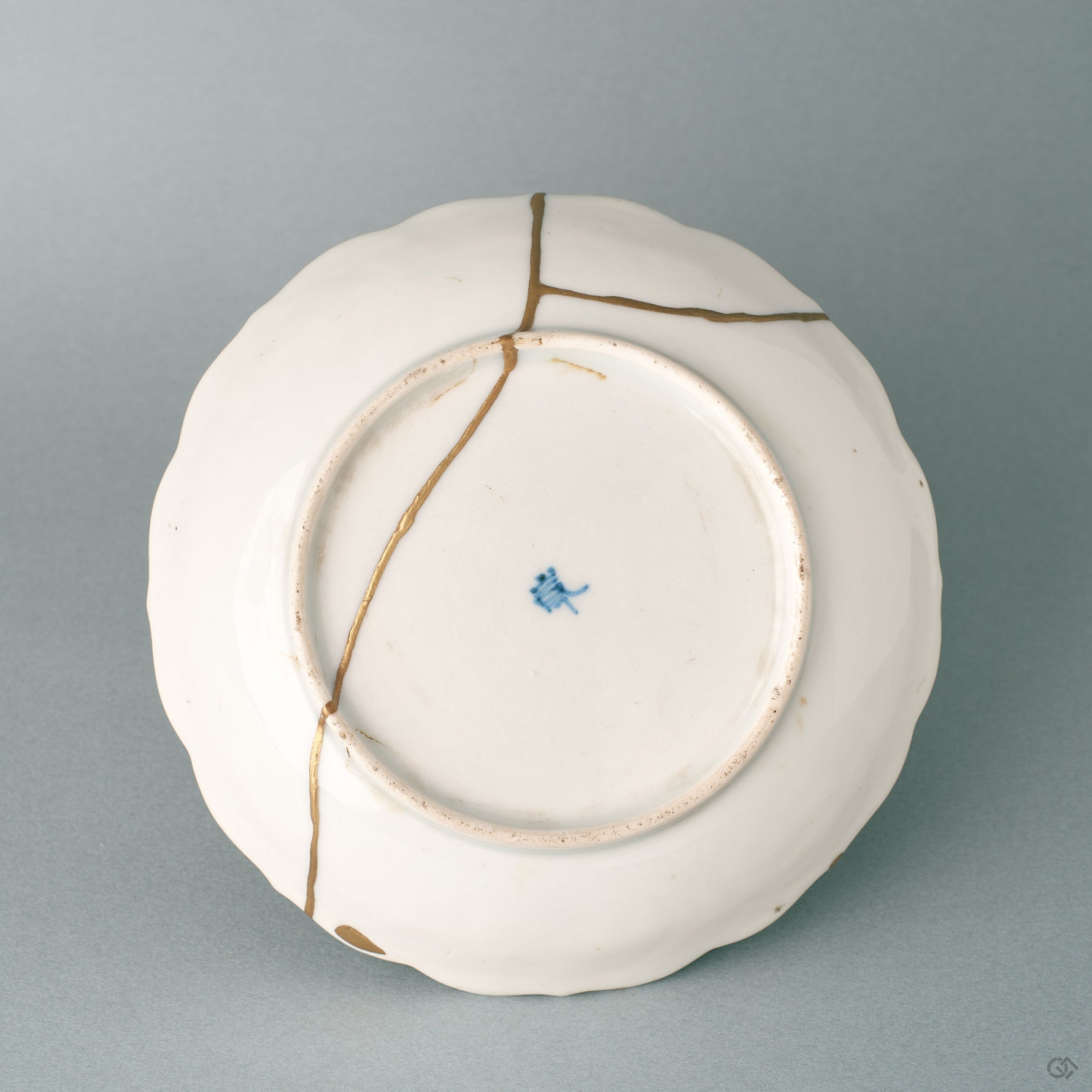 The base of a Ko-Imari kintsugi bowl in white porcelain, where slow craft and a foliate rim reveal its export-ware origins.