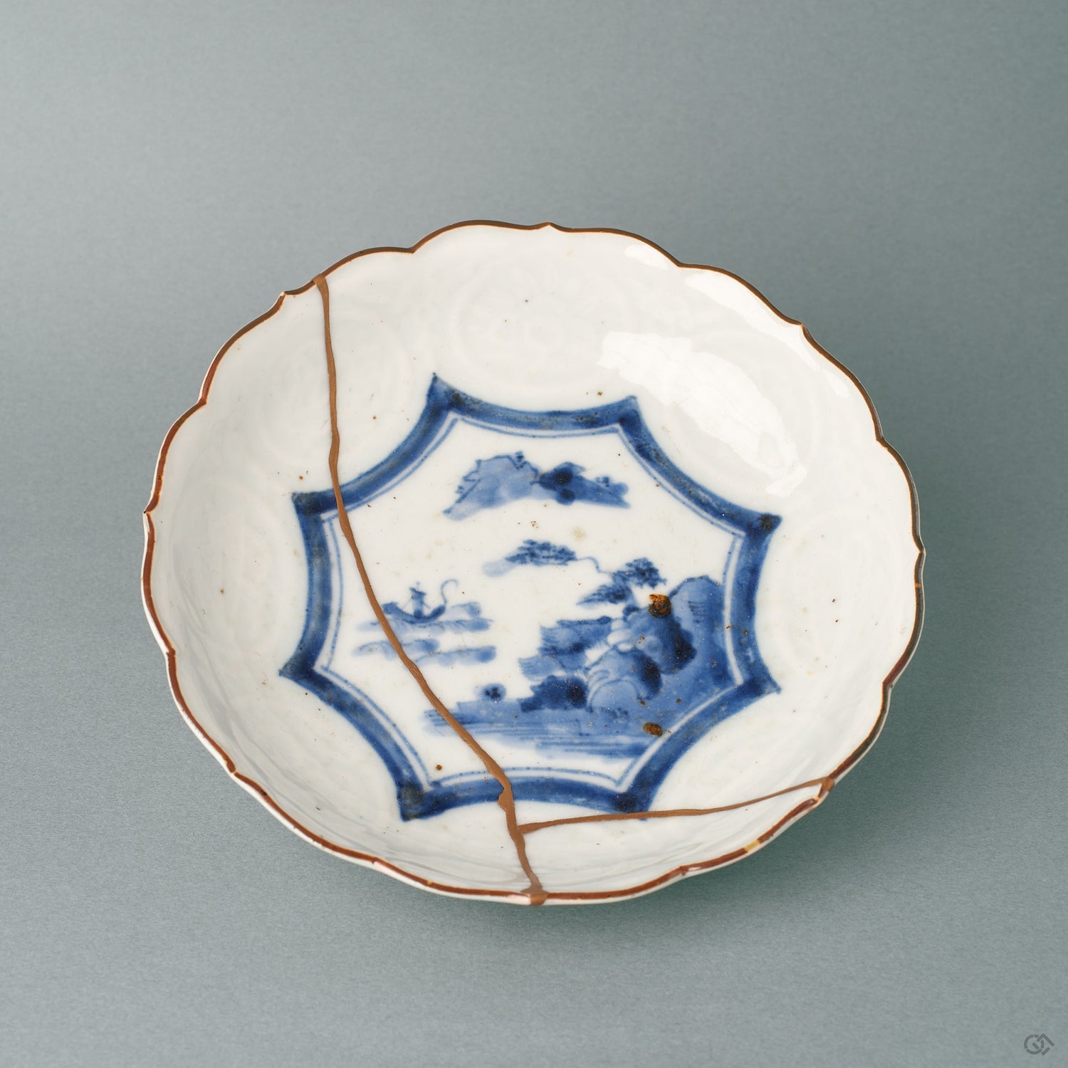 Front view of a Ko-Imari kintsugi bowl, a single 24K gold seam crossing its cobalt landscape, a quiet beauty in white porcelain.