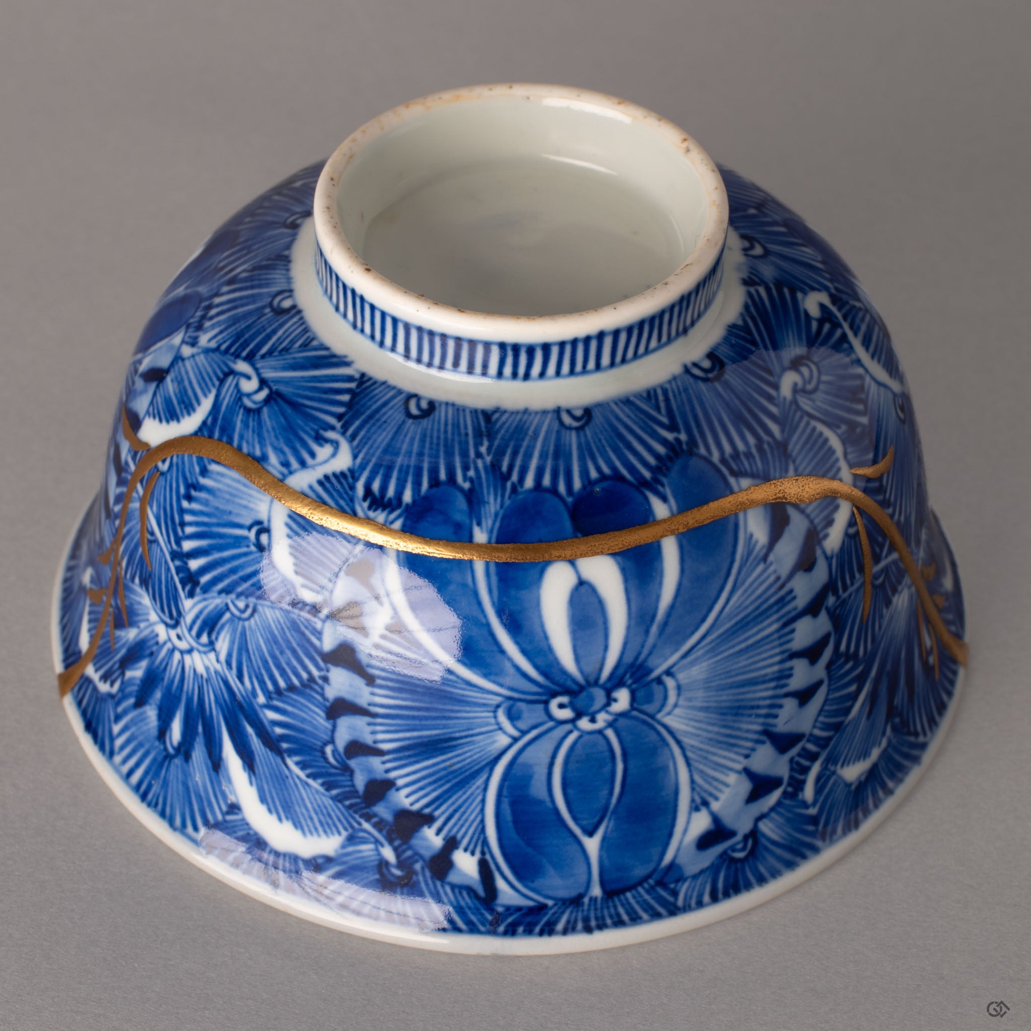 Lower angle of a Ko-Imari kintsugi bowl showing the striped foot and sometsuke botanicals with gold lines, crafted resilience.