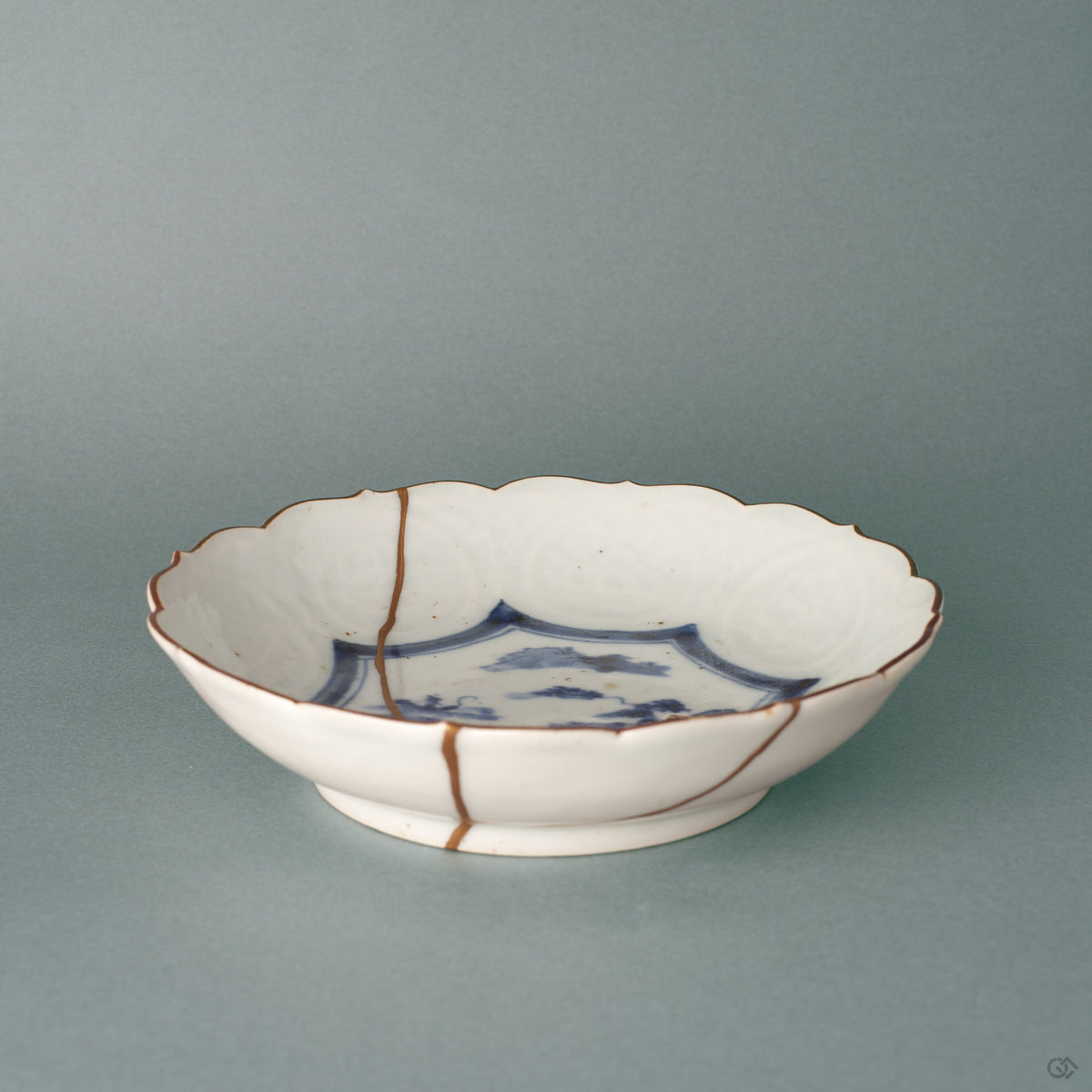 A kintsugi Ko-Imari bowl from a low angle, the single gold seam following its profile, history made visible across white porcelain.