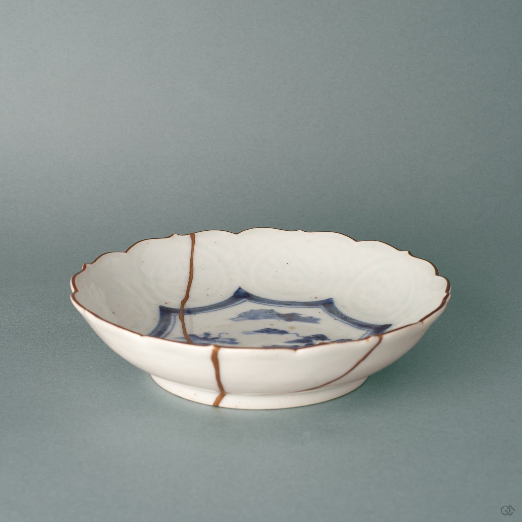 A kintsugi Ko-Imari bowl from a low angle, the single gold seam following its profile, history made visible across white porcelain.