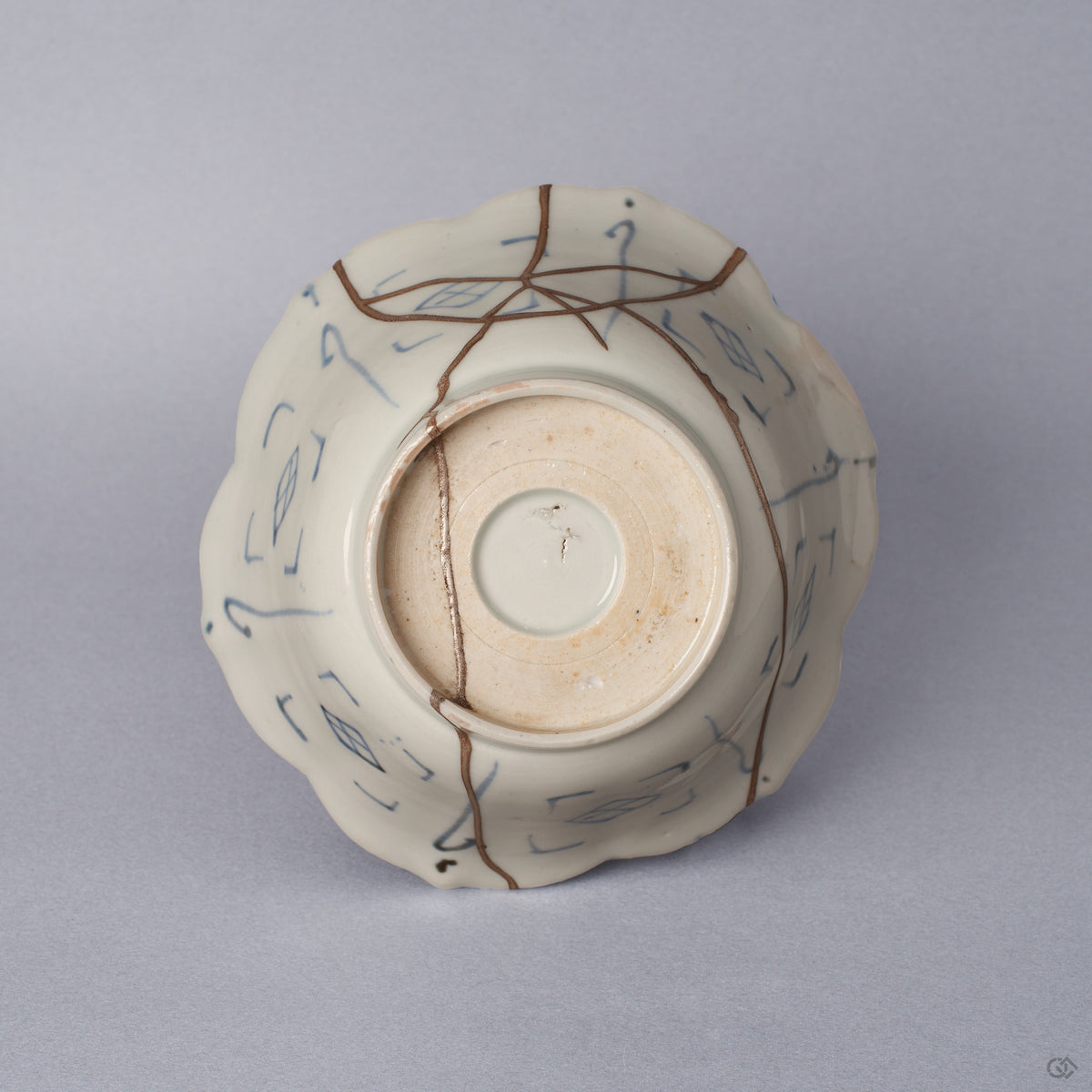 Underside of a Ko-Imari kintsugi bowl, unglazed foot ring and blue lattice motifs crossed by pure silver kintsugi seams, restored with natural urushi in Japan.