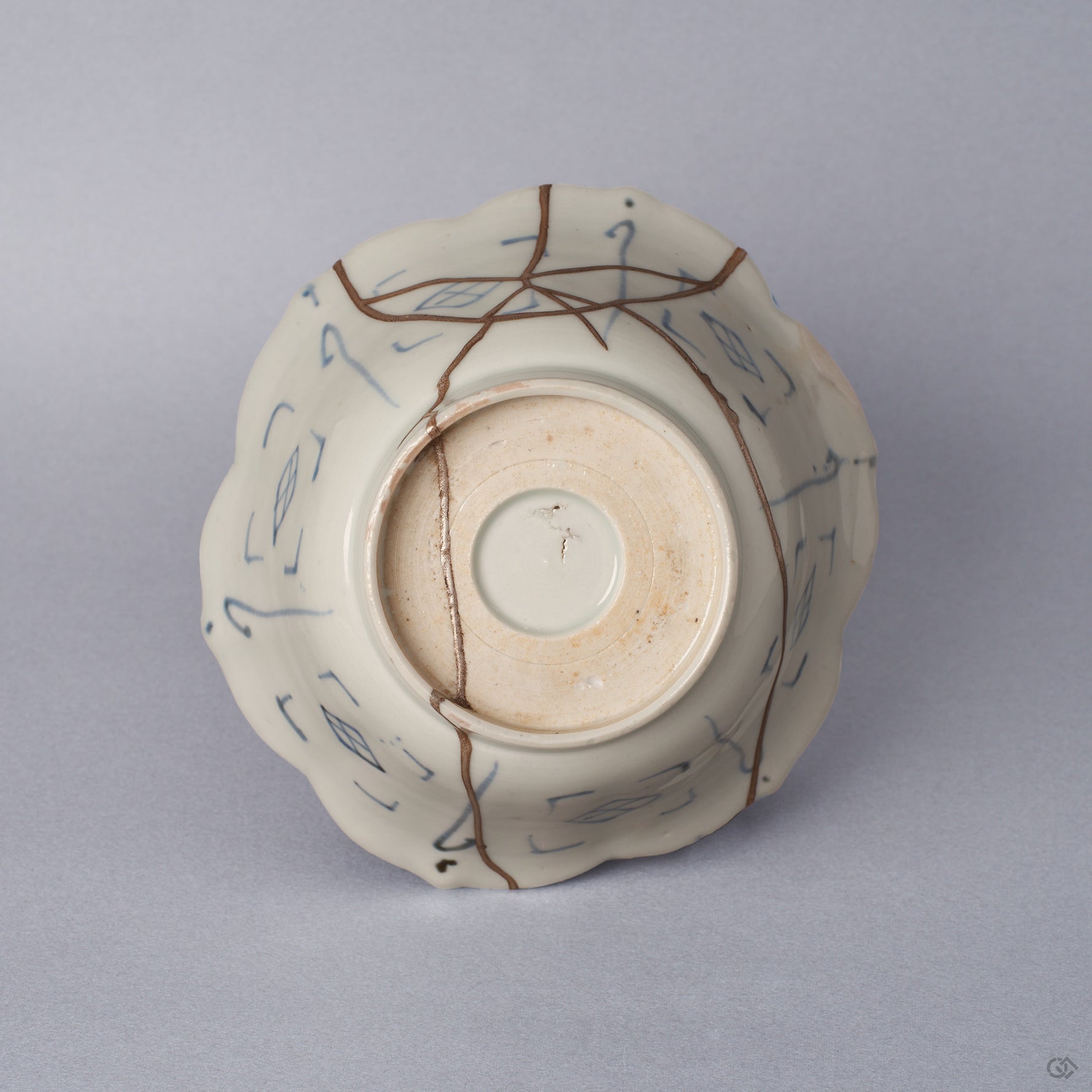 Underside of a Ko-Imari kintsugi bowl, unglazed foot ring and blue lattice motifs crossed by pure silver kintsugi seams, restored with natural urushi in Japan.