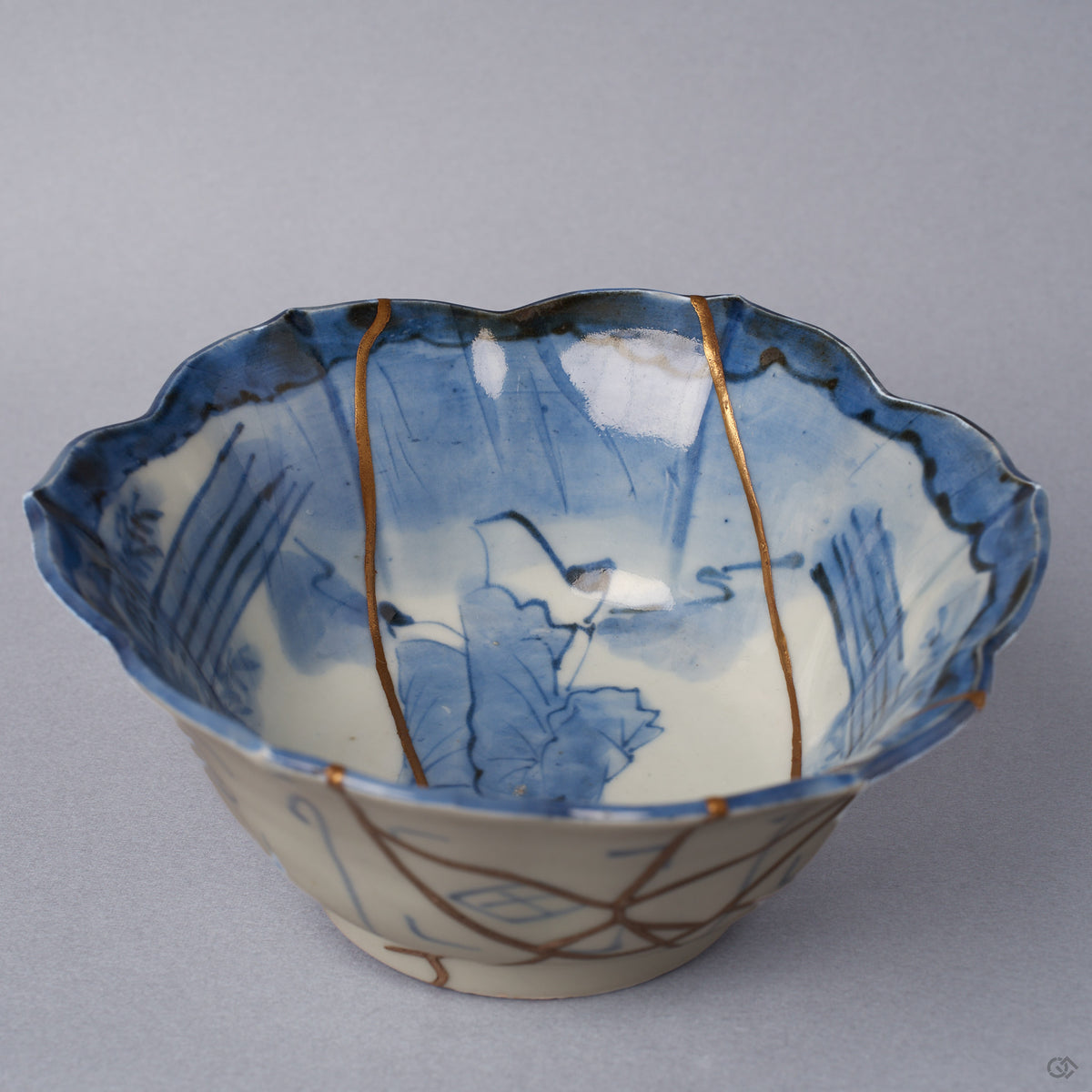 Close view inside a Ko-Imari kintsugi bowl, cobalt lotus and reed painting crossed by fine 24K gold seams converging toward the center, restored with natural urushi in Japan.