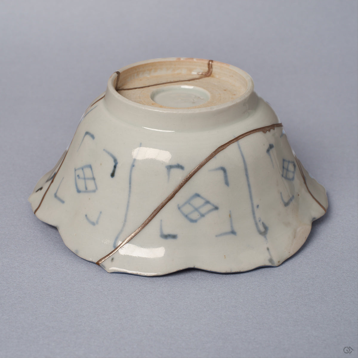 Angled side view of a Ko-Imari kintsugi bowl, pale porcelain exterior with blue lattice motifs and a pure silver seam running from foot to rim, restored with natural urushi.