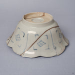 Angled side view of a Ko-Imari kintsugi bowl, pale porcelain exterior with blue lattice motifs and a pure silver seam running from foot to rim, restored with natural urushi.