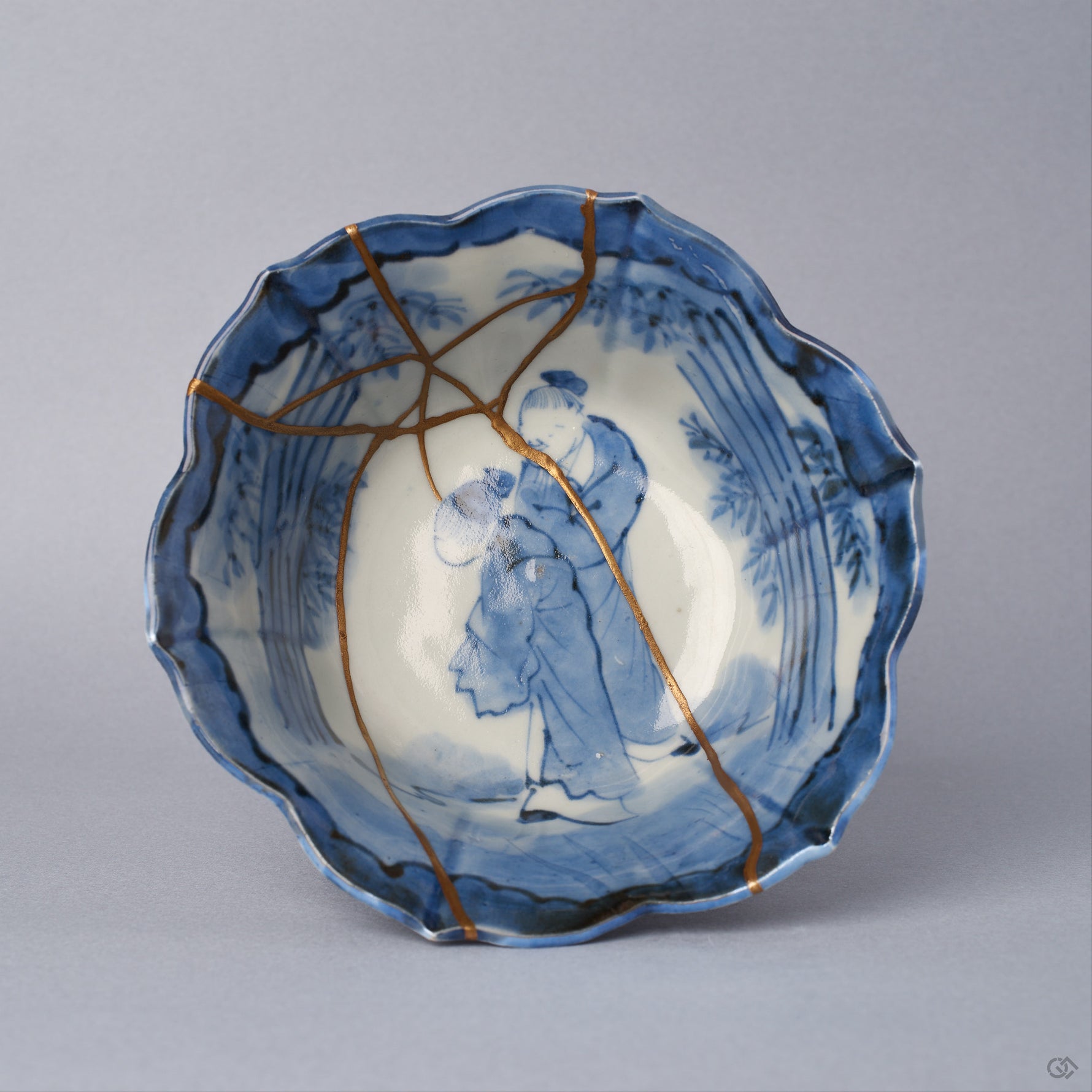 Top view into a Ko-Imari kintsugi bowl, two cobalt figures — a sage and attendant among bamboo — framed by 24K gold seams converging at the center, restored with natural urushi.