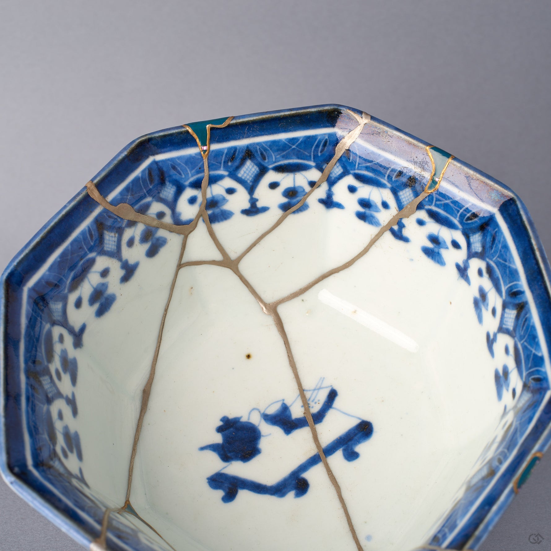 Interior close-up of the Ko-Imari bowl, a rim loss filled with green urushi edged in 24K gold, with a pure silver kintsugi seam running down into the pale porcelain well.