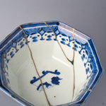 Second interior close-up of the octagonal bowl, green-urushi rim fill and gold outline above the blue net-and-blossom border, silver seams crossing toward the central floral spray.