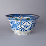 Side view of the Ko-Imari bowl showing two wide rim losses filled with green urushi and raden, gold-outlined, above blue lotus cartouches, with silver kintsugi seams across the porcelain.