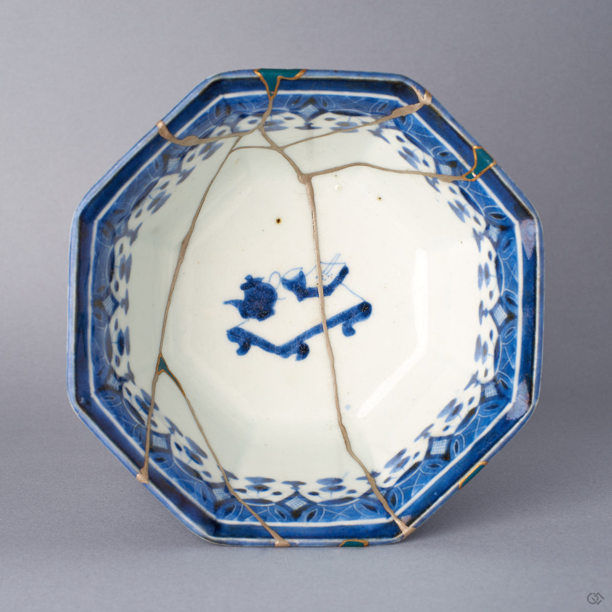 Top-down view into the octagonal Ko-Imari bowl, green-urushi and gold rim fills around the deep blue border, silver kintsugi seams branching across the interior to the central blue motif.