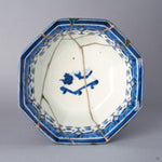 Top-down view into the octagonal Ko-Imari bowl, green-urushi and gold rim fills around the deep blue border, silver kintsugi seams branching across the interior to the central blue motif.