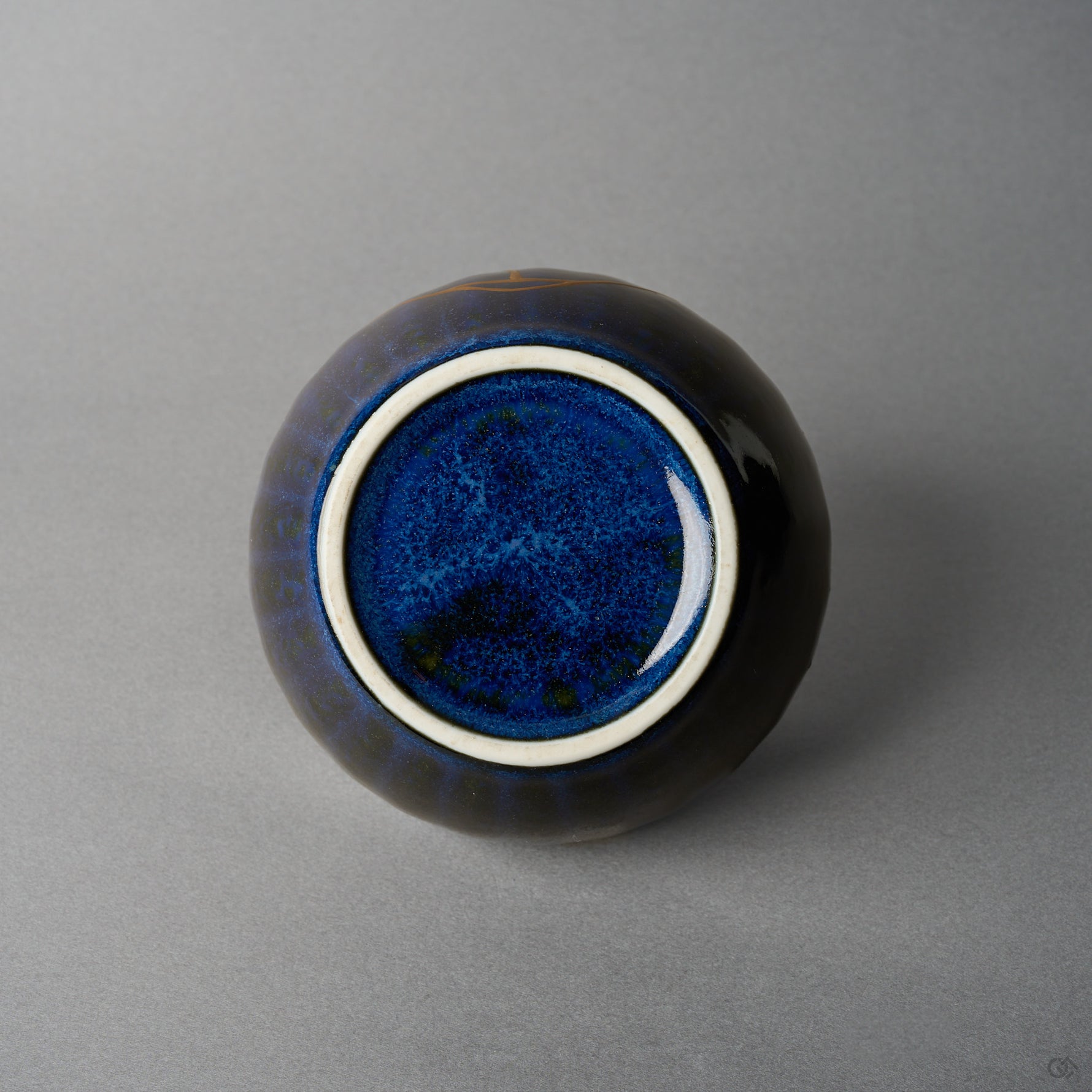 Kintsugi bowl base with white foot ring and speckled night-blue glaze, the gold urushi seam visible at the upper edge.