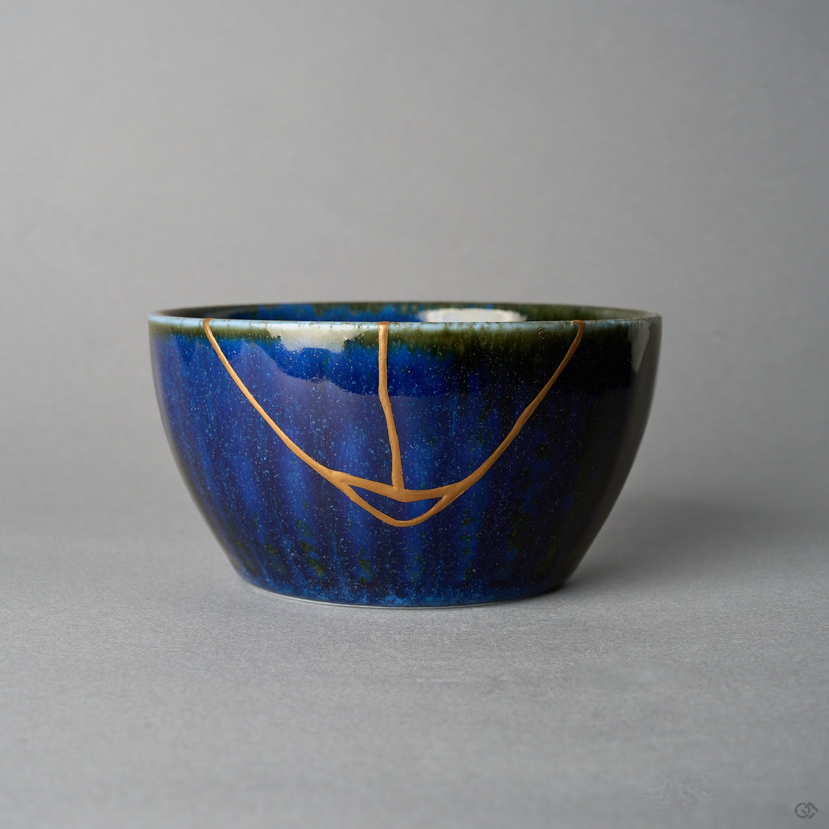 Japanese kintsugi bowl in Mino ware: a V-shaped seam of urushi and 24K gold crosses the starry night-blue kamahen glaze to the olive-green rim, front view.
