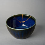 Kintsugi bowl interior where three branches of the urushi and 24K gold seam meet in a small loop on the starry night-blue glaze, close-up view.