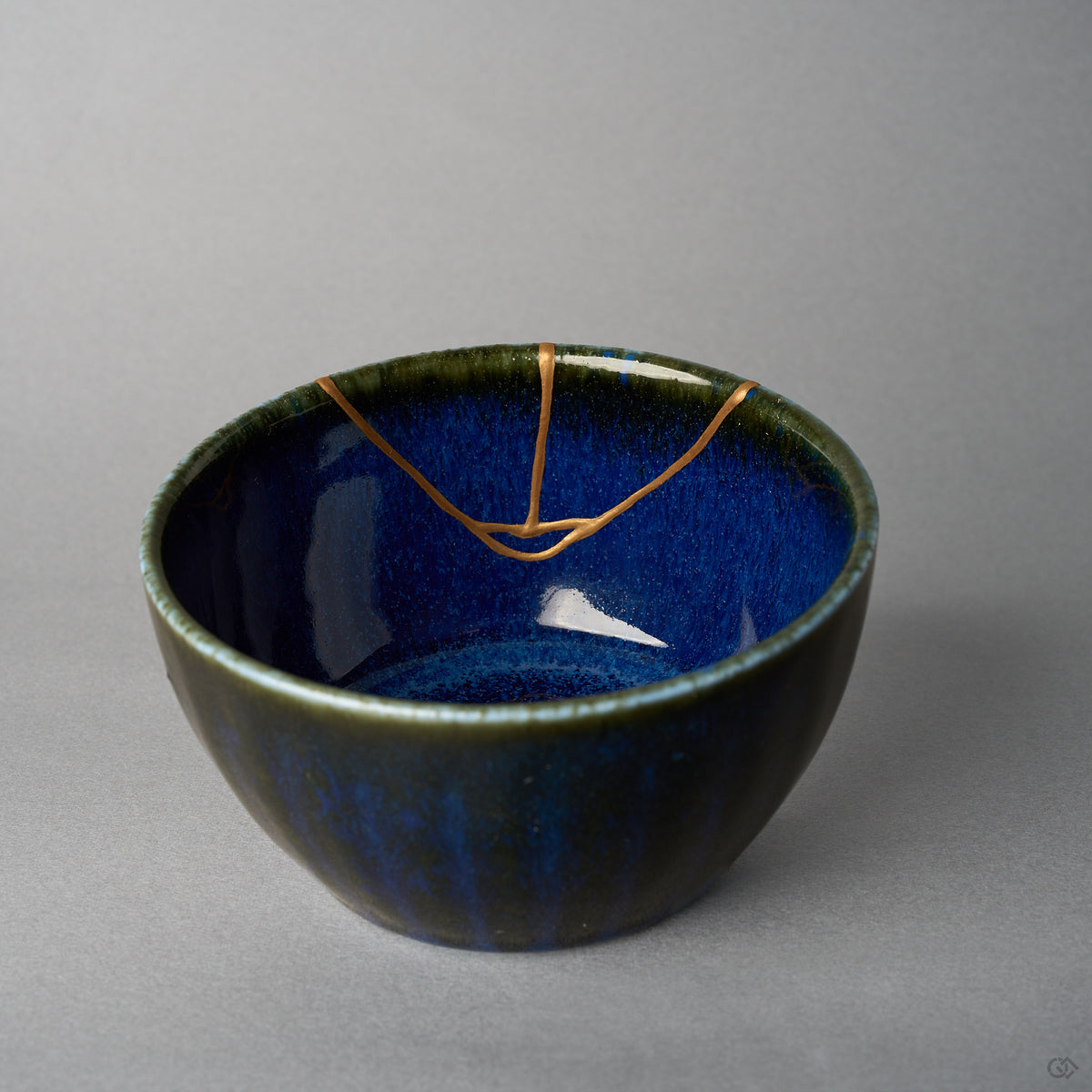 Kintsugi bowl interior where three branches of the urushi and 24K gold seam meet in a small loop on the starry night-blue glaze, close-up view.