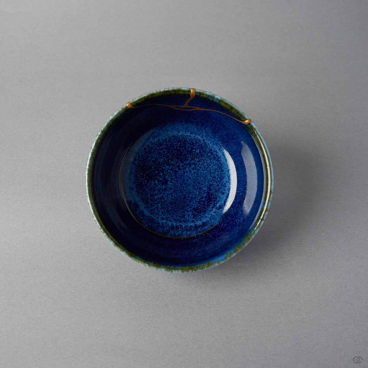 Kintsugi bowl seen from above; the urushi and 24K gold seam crosses the olive-green rim and branches onto the starry night-blue interior.