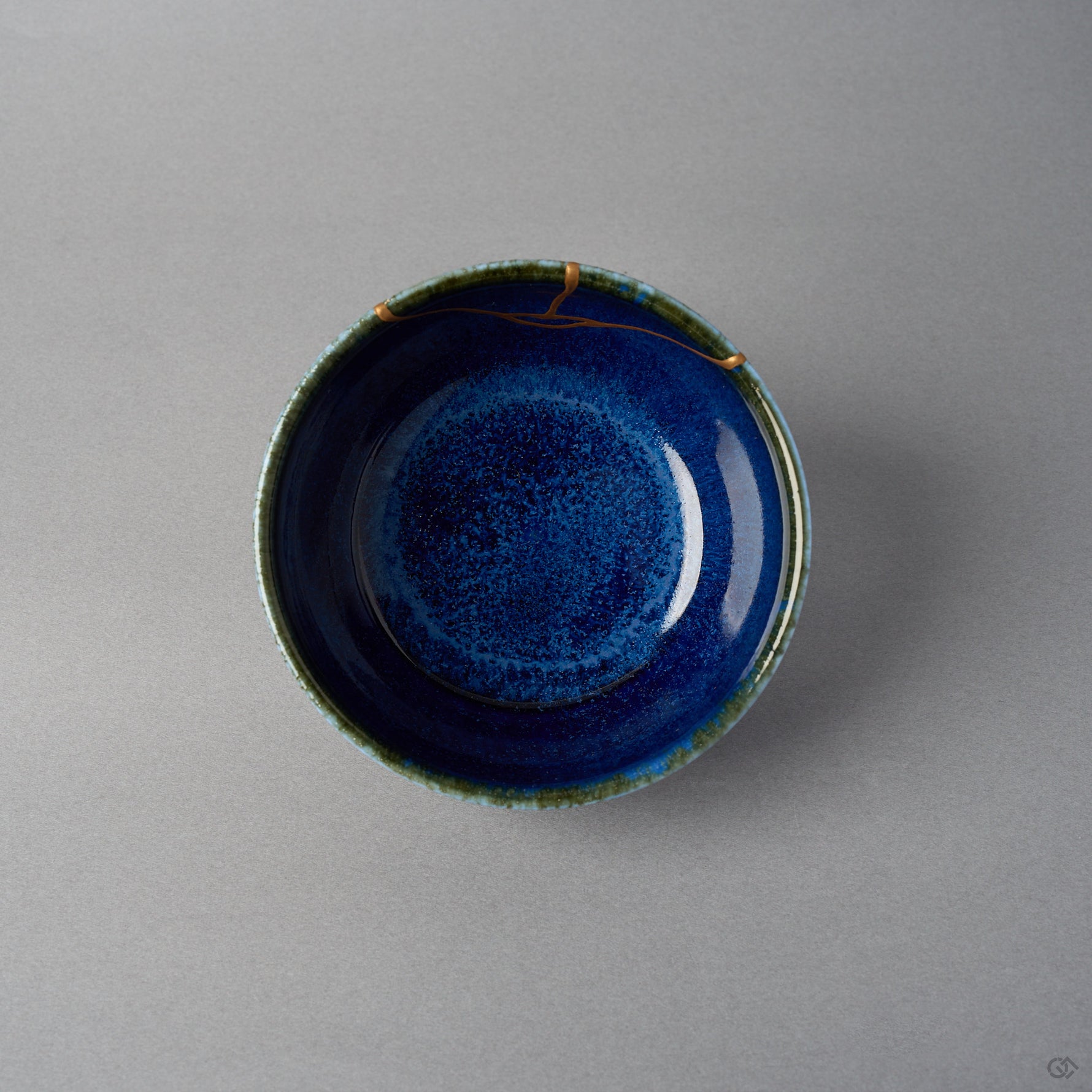 Kintsugi bowl seen from above; the urushi and 24K gold seam crosses the olive-green rim and branches onto the starry night-blue interior.