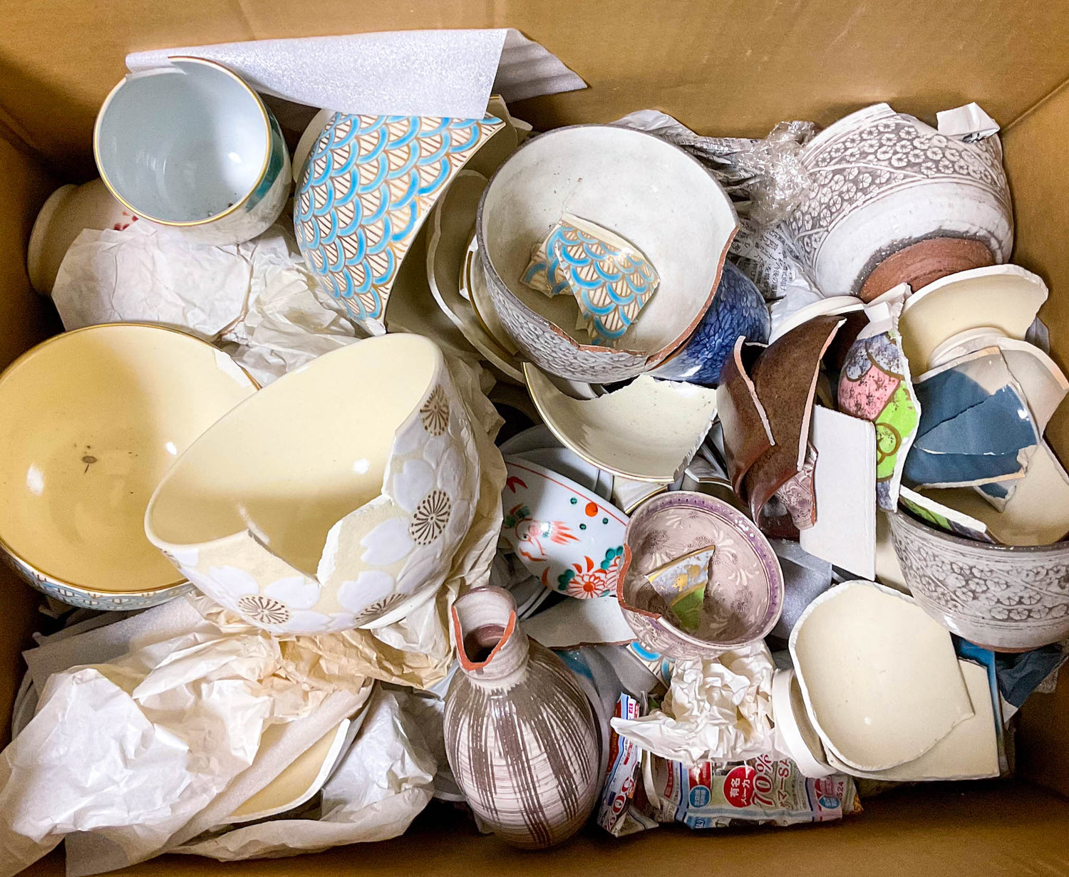 Cardboard box filled with broken Kyoto ware matcha bowls and cups sourced from Japanese kilns for sustainable kintsugi restoration.