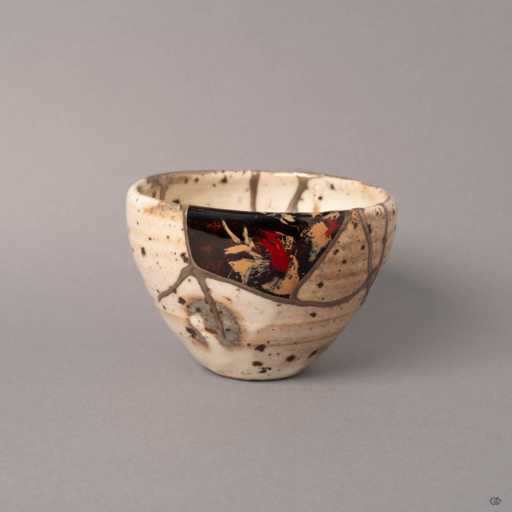 Kintsugi Shigaraki earthenware cup from the front, ivory white body with dark iron speckles and pure silver seams joining reassembled fragments, urushi-e panel of red and gold brushwork on black lacquer near the rim.