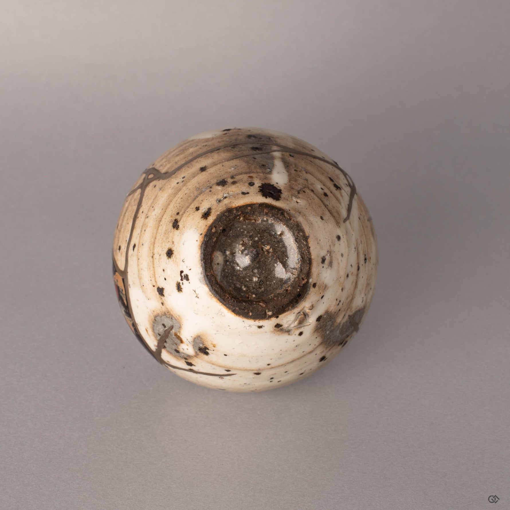 Bottom view of a kintsugi Shigaraki earthenware cup showing the unglazed foot ring and base, silver restoration lines visible where fragments meet the underside.