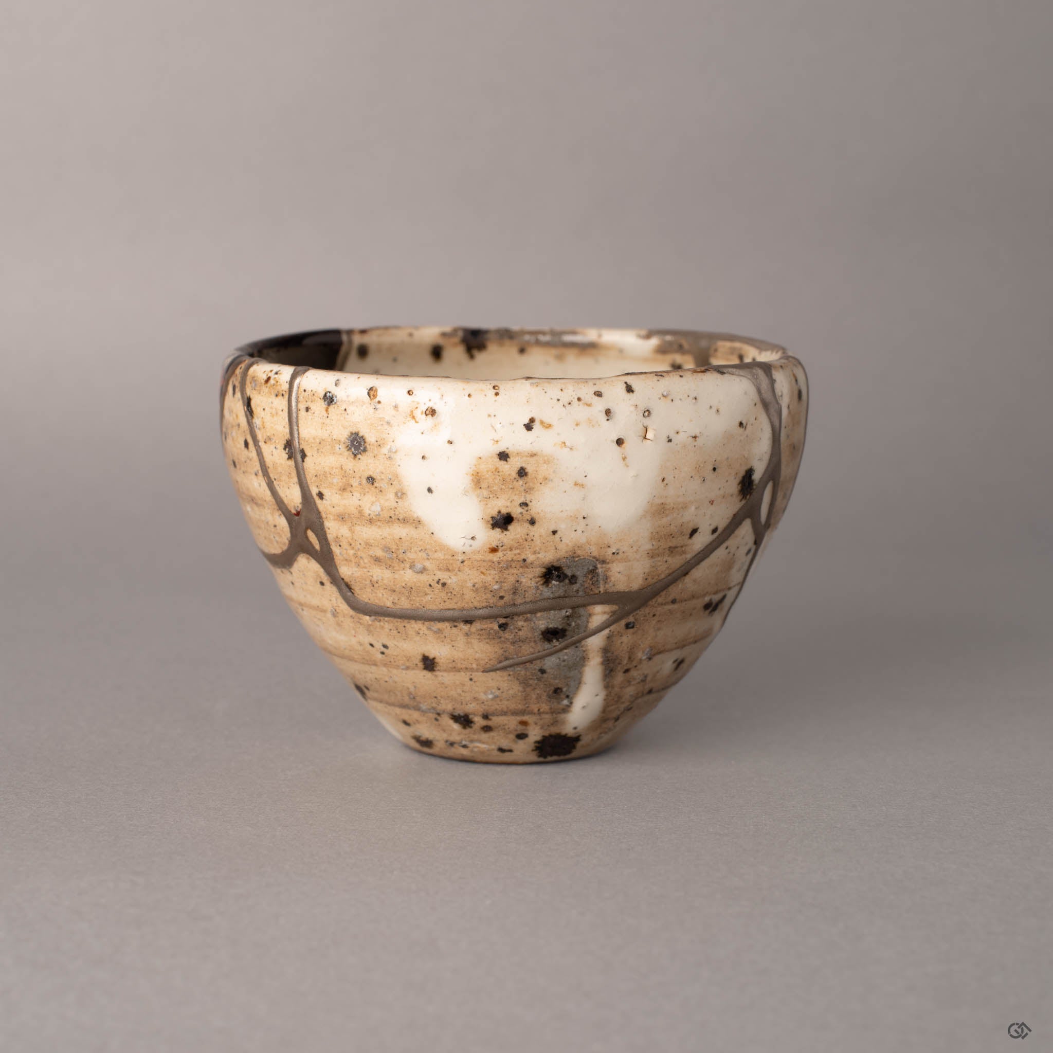 Third side view of a kintsugi Shigaraki cup with silver restoration seams, the organic shape of the hand-thrown vessel catching soft light across its speckled surface.