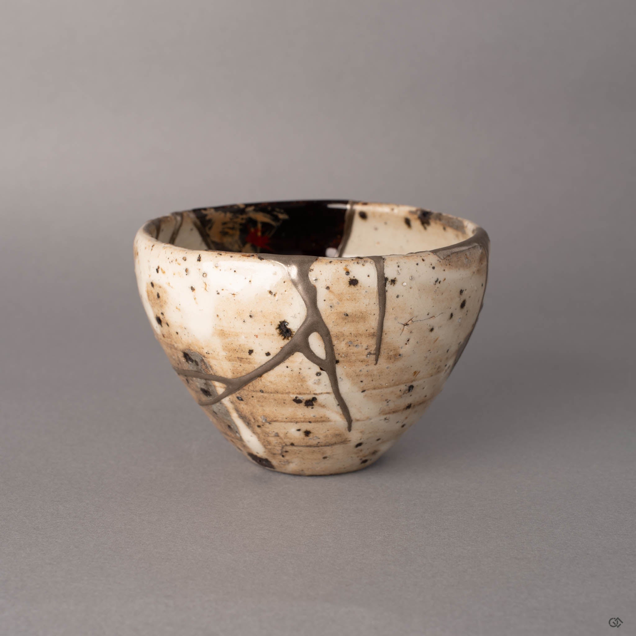 Kintsugi Shigaraki cup from a second side angle, pure silver lines following the fracture path across the robust rounded form, dark iron spots scattered over the white earthenware.