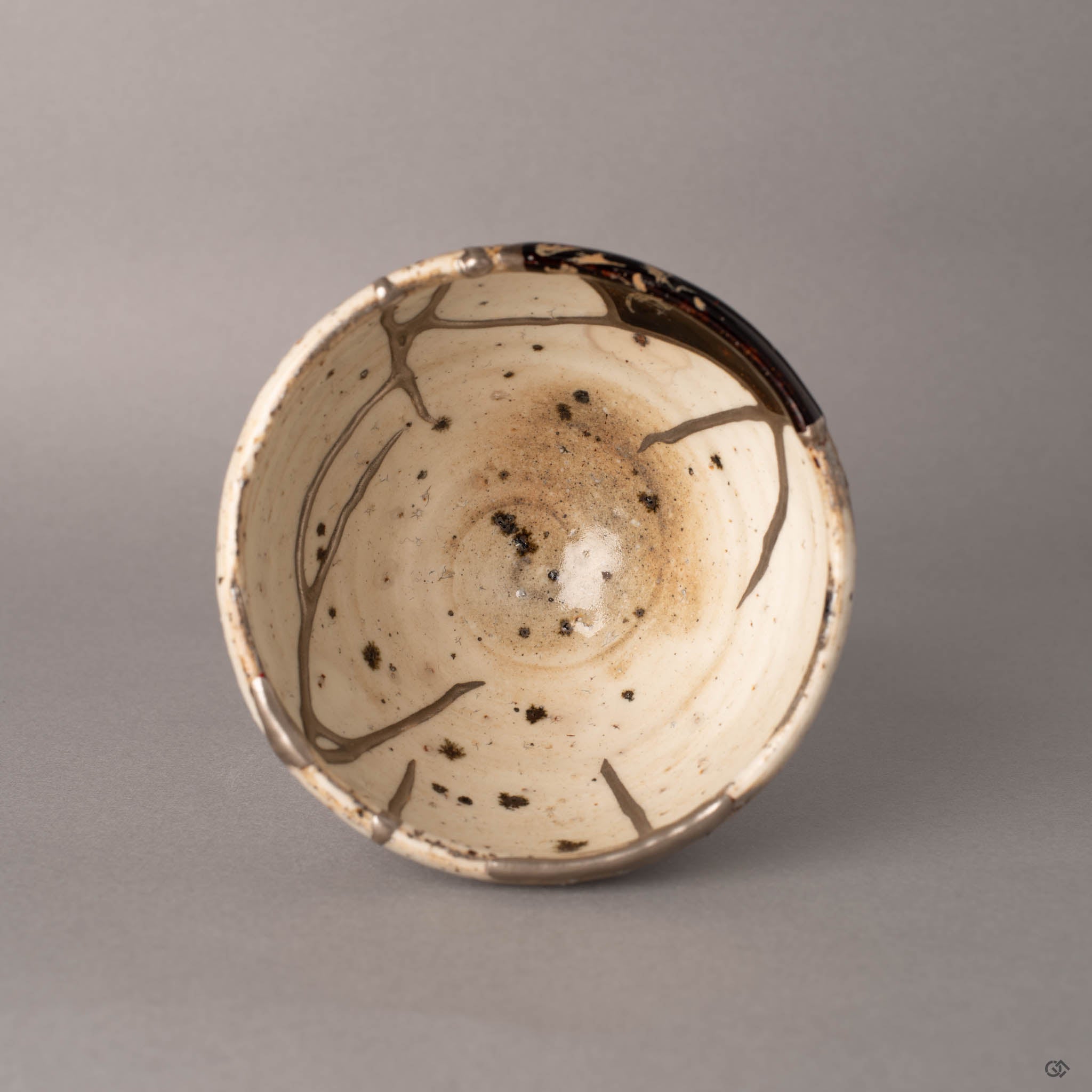 Top view of a kintsugi Shigaraki cup, silver seams radiating across the interior alongside the urushi-e panel, the full pattern of restoration visible from above.