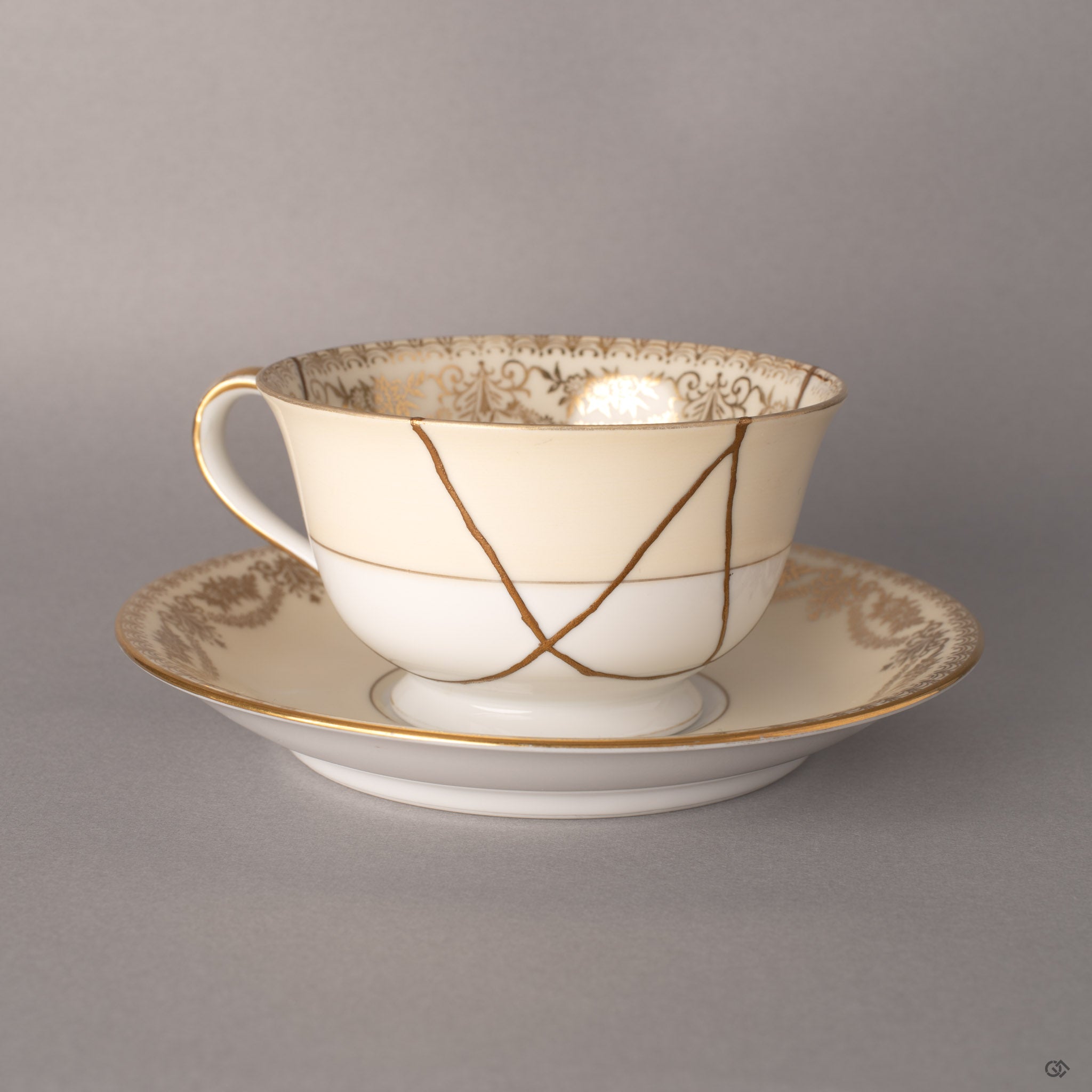 Early Noritake cup and saucer with 24K gold kintsugi seams tracing mended fractures, Art Deco florals beneath.