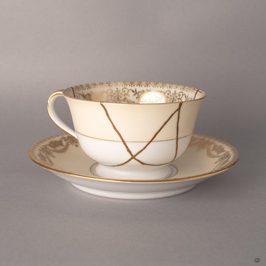 Early Noritake cup and saucer with 24K gold kintsugi seams tracing mended fractures, Art Deco florals beneath.