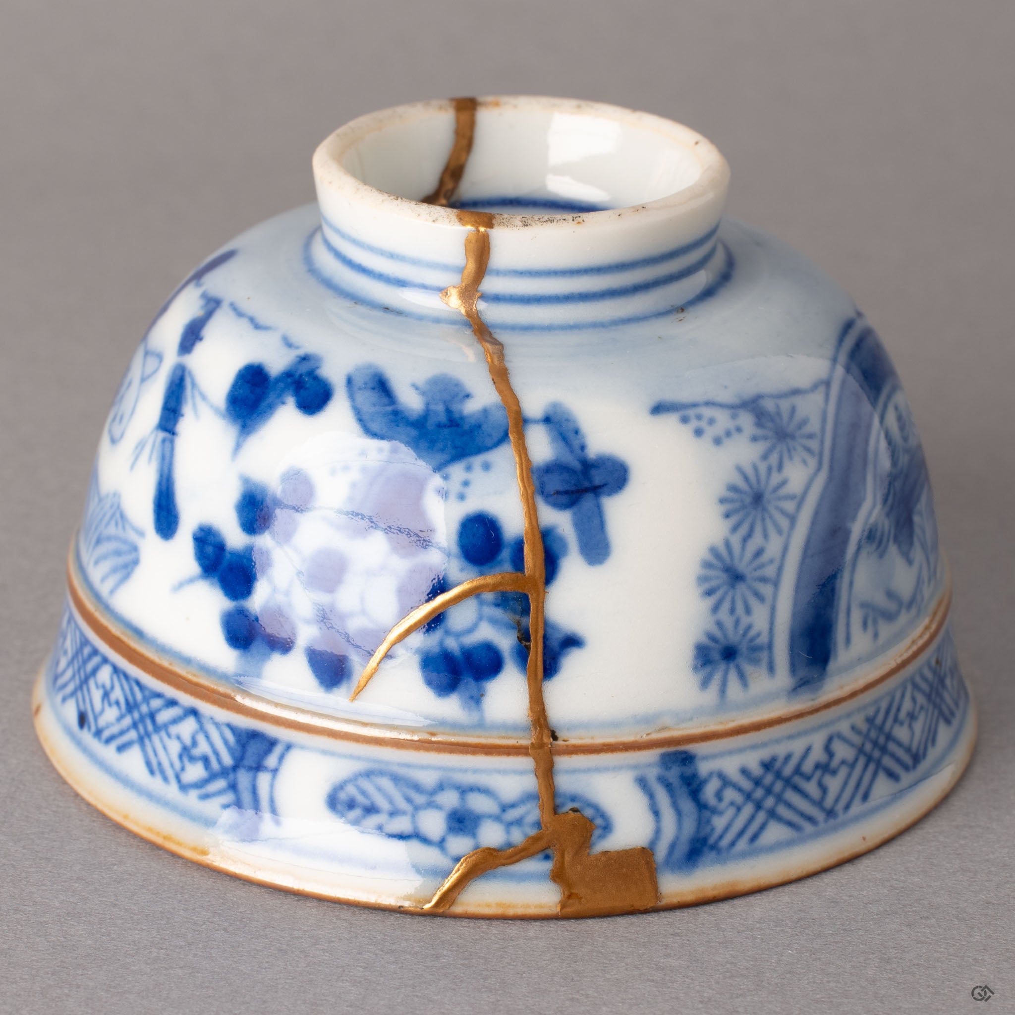 Close-up of kintsugi gold seam on Ko-Imari porcelain where restoration meets sometsuke blue floral painting, urushi beneath the surface.