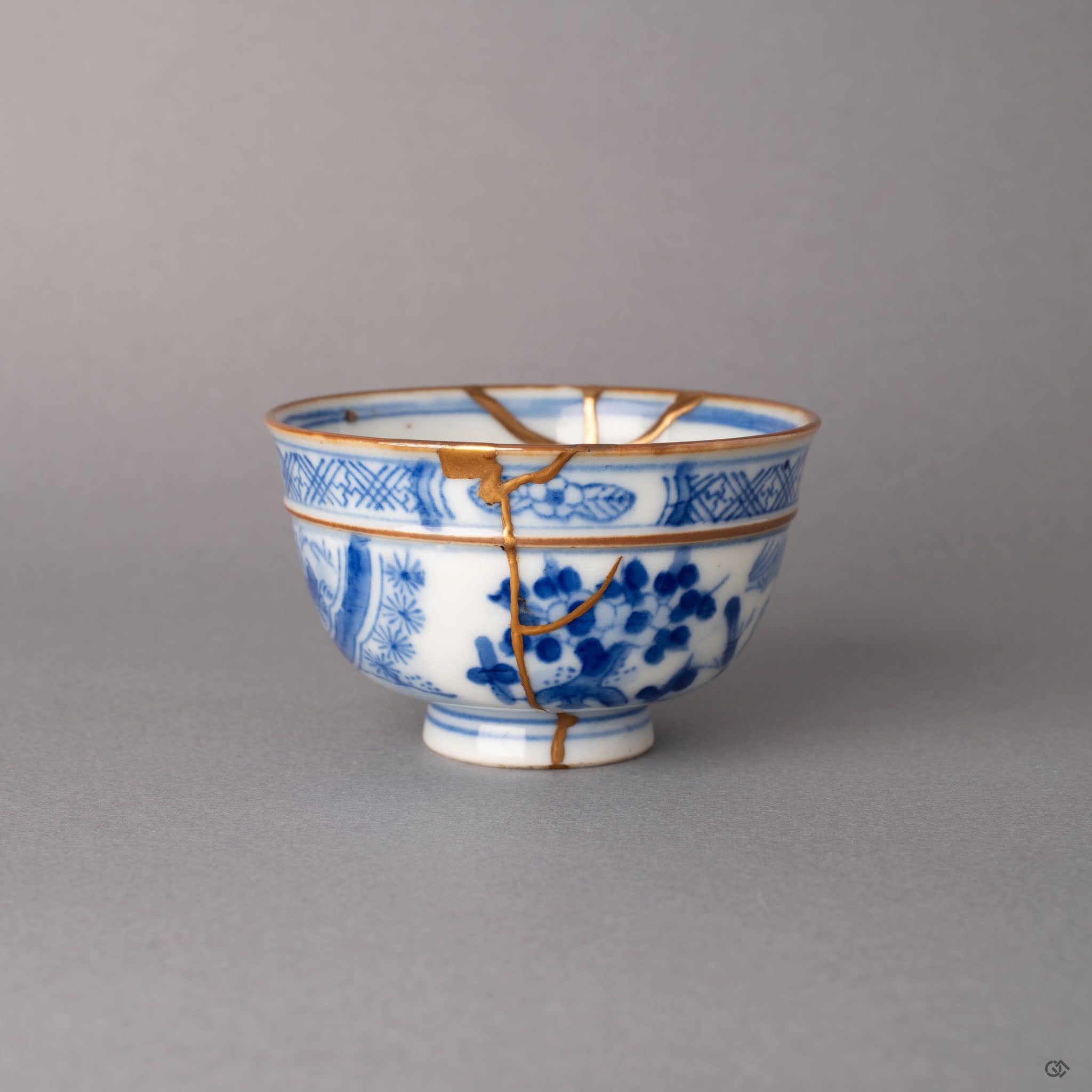 Kintsugi Ko-Imari sometsuke cup with gold seams crossing hand-painted blue floral motifs on white porcelain, history made visible.