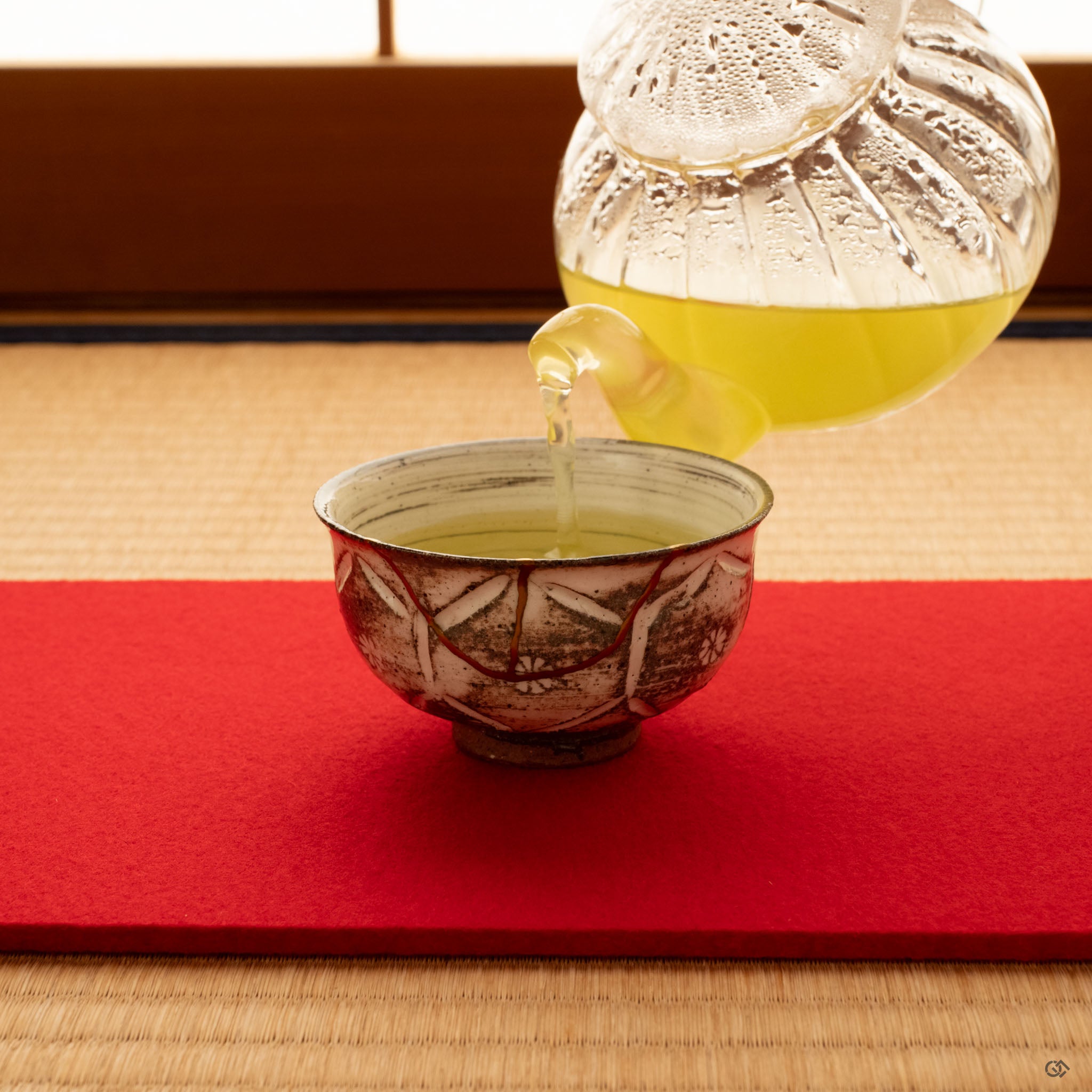 Green tea poured into a kintsugi Kyoto cup from a glass teapot, gold seams glowing softly as a moment of contemplation takes shape.