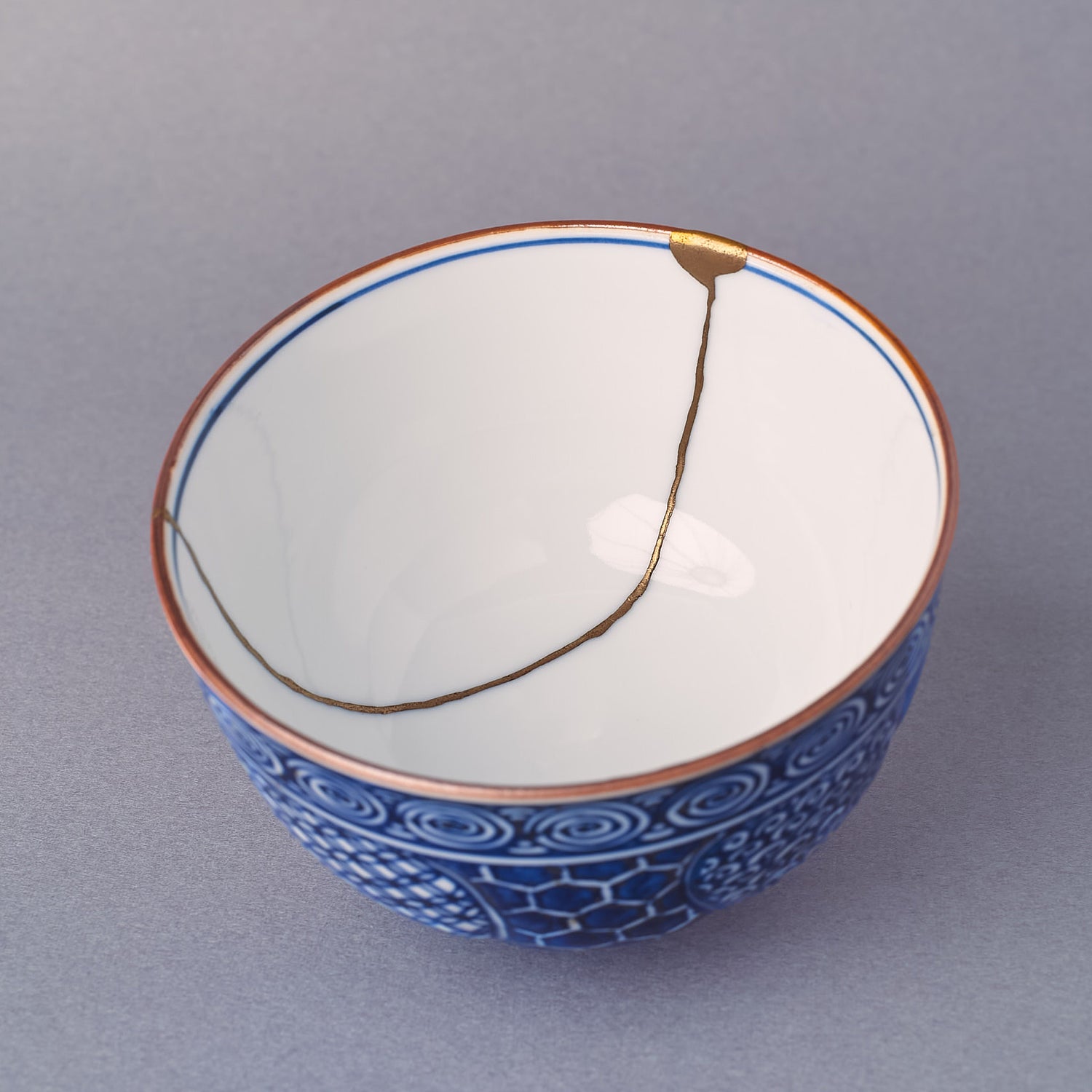 Interior close-up of the Kyoto ware porcelain cup, white glaze and sometsuke blue rim, 24K gold kintsugi seam meeting the lip, lidded teacup form.
