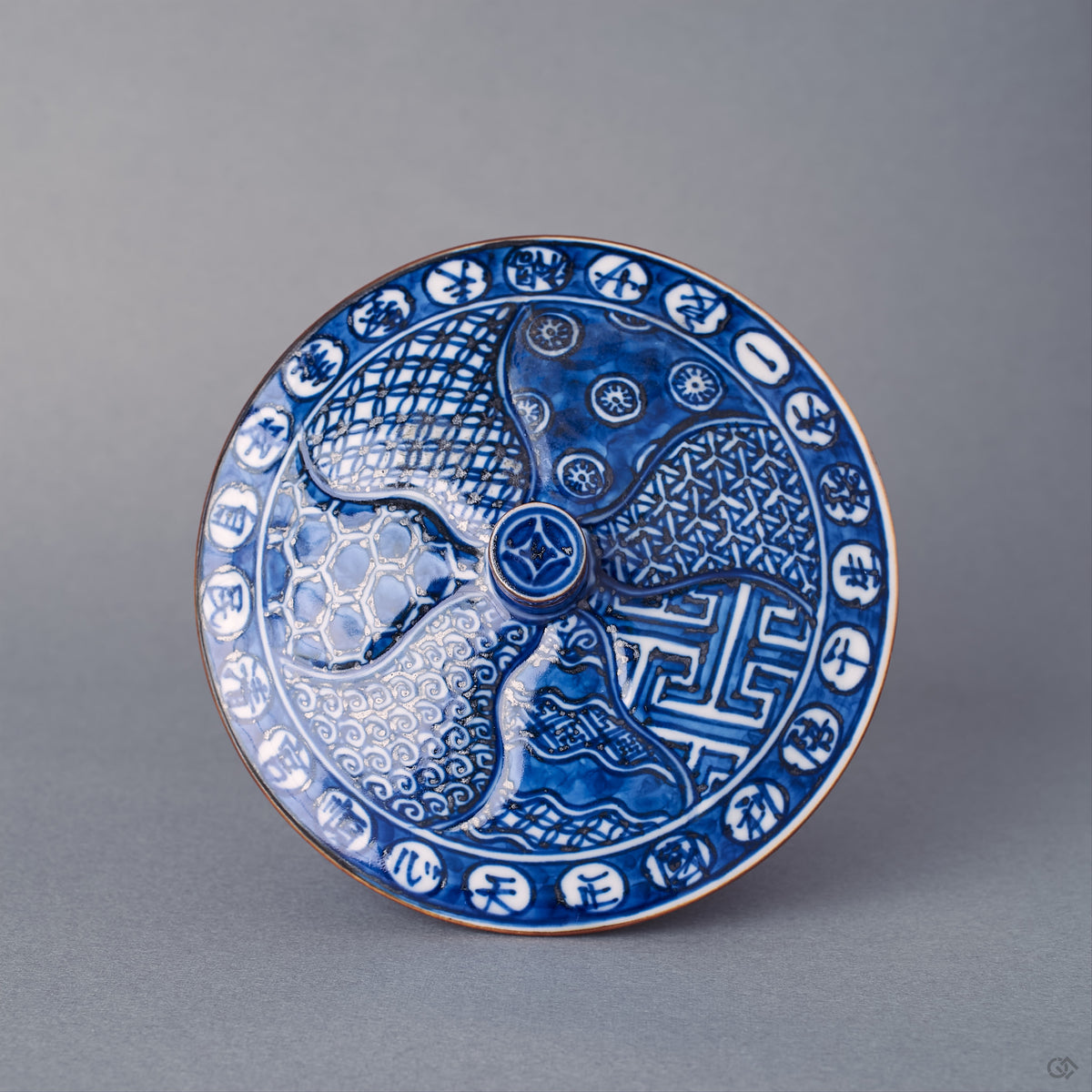 Top view of the cup's domed lid, sometsuke cobalt blue swirl and roundel komon, gold-ringed knob, 24K gold finishing along the lid restoration.