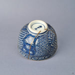 Side view of a Kyoto ware kintsugi cup, sometsuke blue with key-fret and basket-weave bands, 24K gold seam tracing the break, fitted lid.