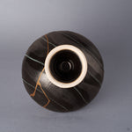 Underside view of a black Arita ware footed bowl showing the striped glaze and the cream unglazed foot rim, with the 24K gold kintsugi seam running down toward the pedestal.