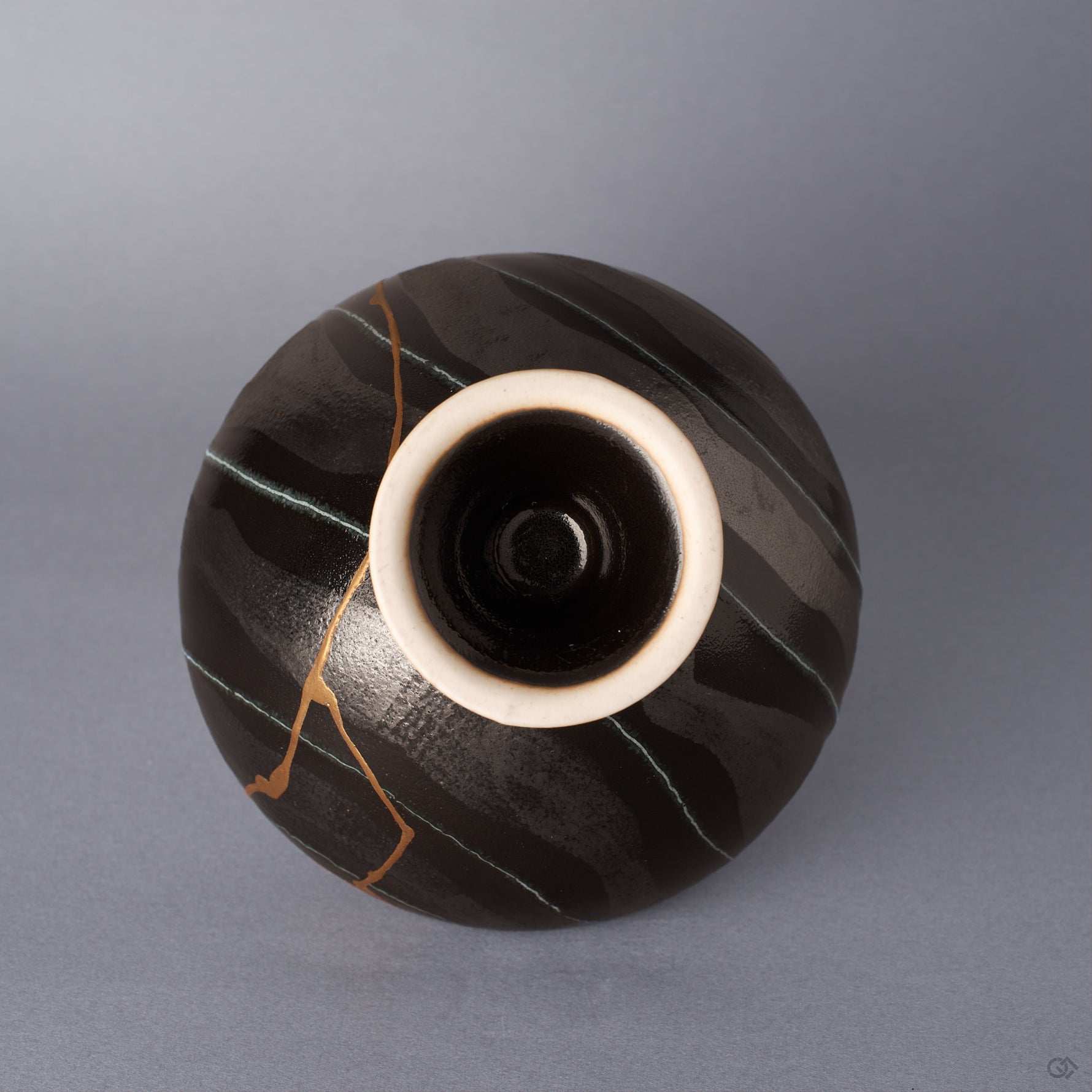 Underside view of a black Arita ware footed bowl showing the striped glaze and the cream unglazed foot rim, with the 24K gold kintsugi seam running down toward the pedestal.