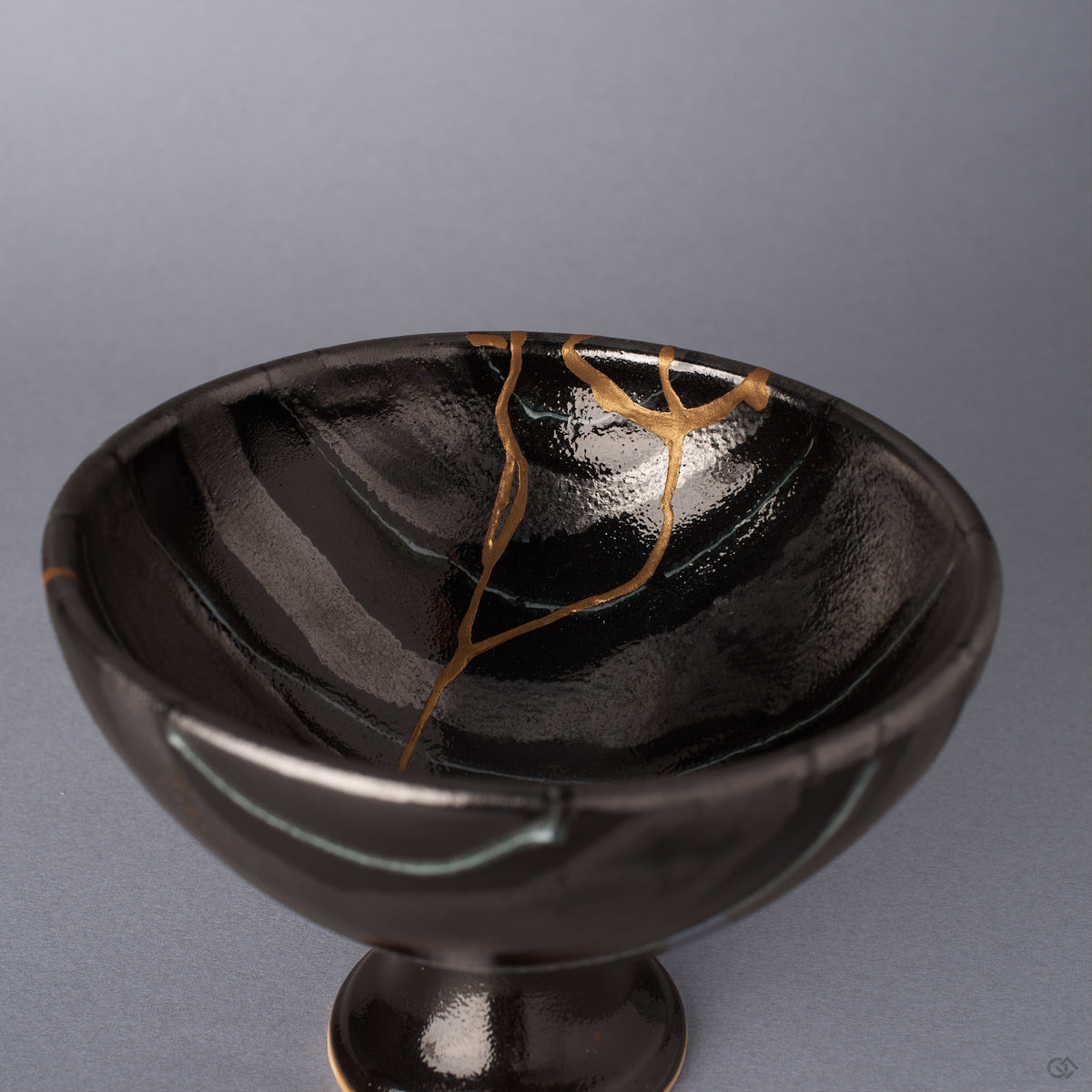 Close view of the interior of a black Arita ware footed bowl, the 24K gold kintsugi seam branching near the rim across the glossy striped glaze in varying tones.