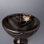 Close view of the interior of a black Arita ware footed bowl, the 24K gold kintsugi seam branching near the rim across the glossy striped glaze in varying tones.