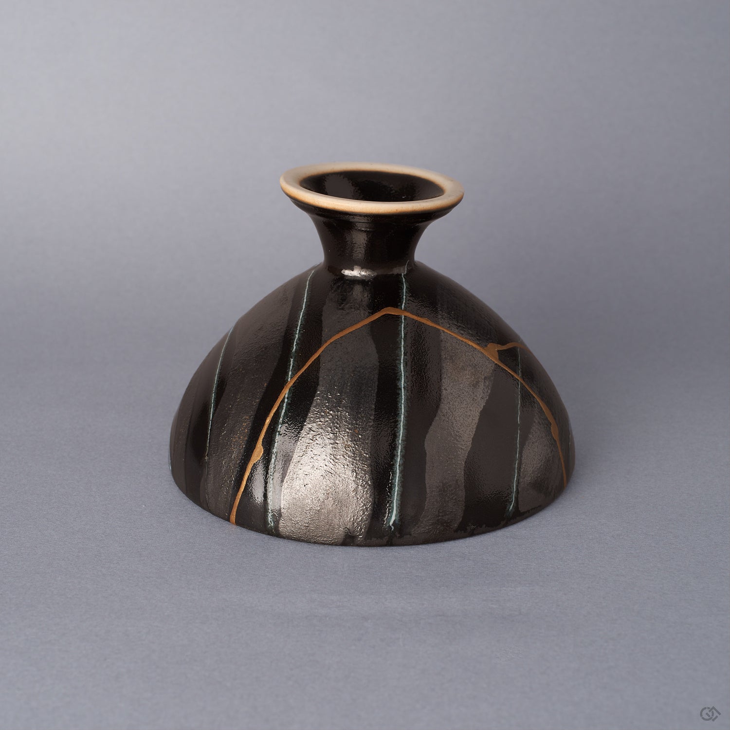 Side view of a black Arita ware footed bowl, the 24K gold kintsugi seam tracing vertically down the striped exterior glaze toward the cream-rimmed pedestal foot.