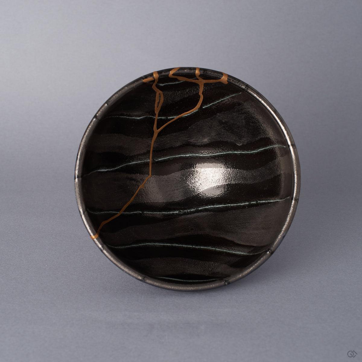 Top view into a black Arita ware footed bowl, the 24K gold kintsugi seam branching across the interior against hand-painted striations in varying shades of black and pewter.